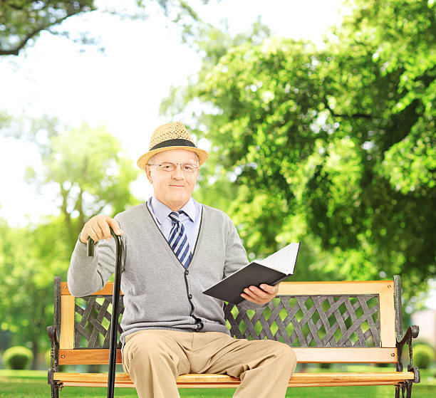 istock Senior man sitting on a wooden bench and reading  book 464323303