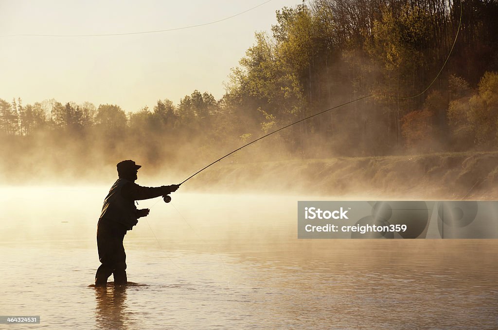 Silhouette of Fly Fisherman in Nova Scotia A fly fisherman fishes for Striped Bass in the early morning fog on a river in Nova Scotia. Fly-fishing Stock Photo