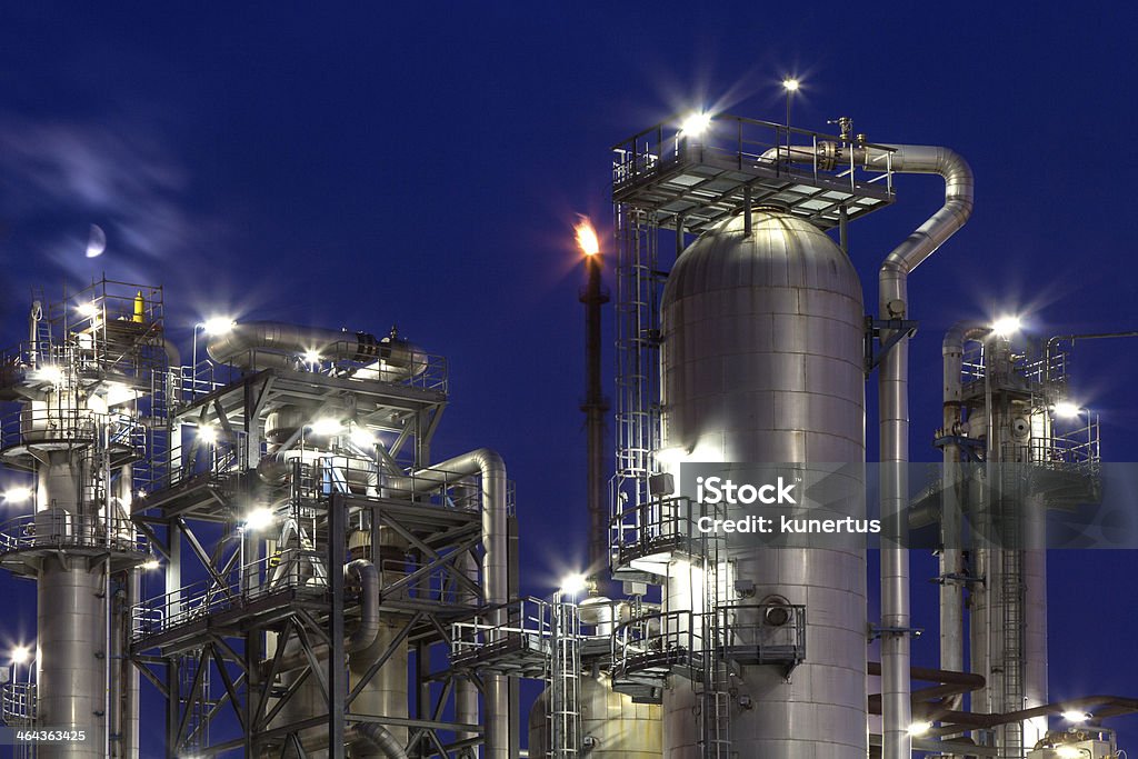 chemical plant and moon An illuminated chemical plant at night with the moon behind some clouds Blue Hour - Twilight Stock Photo