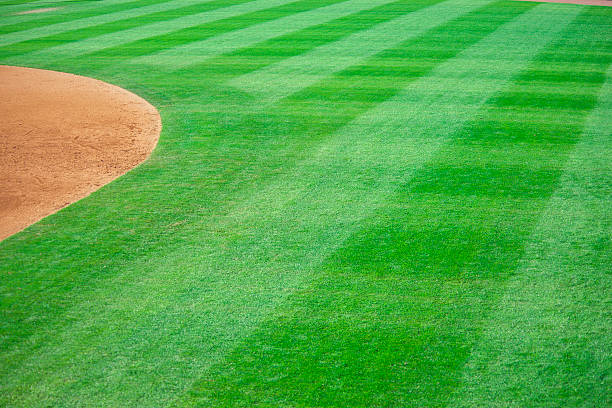 Baseball Outfield of Baseball Field at Baseball Game this photo is of baseball outfield of a baseball field at a baseball game. the outfield is lush green grass or lawn that has been mowed. and there are patterns in the grass. there is also the warning track in the background next to the homerun wall. the photo was taken at a live baseball game or sporting event. the lighting is natural sunlight.      outfield stock pictures, royalty-free photos & images