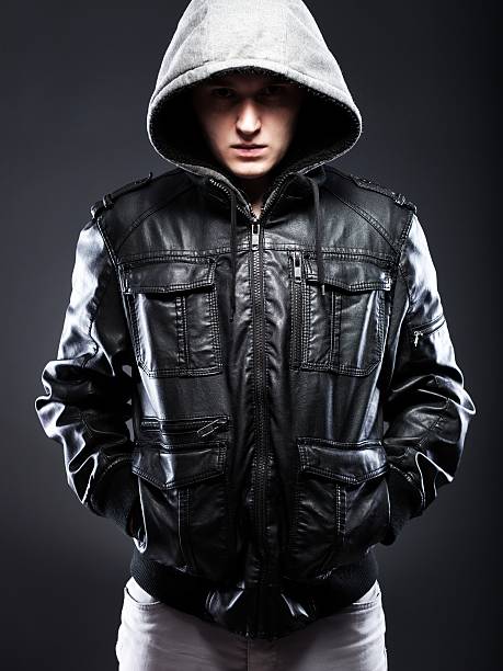 Young man in leather jacket with hood Young man in leather jacket with a hood on darkness background larrikin stock pictures, royalty-free photos & images