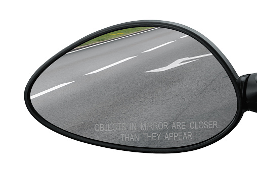 Rear view mirror with warning text objects in mirror are closer than they appear, isolated, reflecting road, left side lateral, macro closeup, tarmac asphalt reflection, white lines, arrows marking