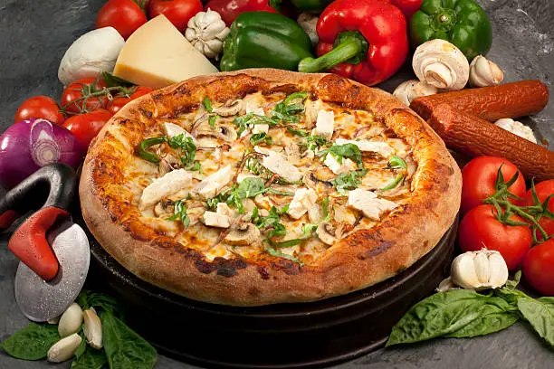 A pizza loaded with ingredients,surrounded with raw ingredients