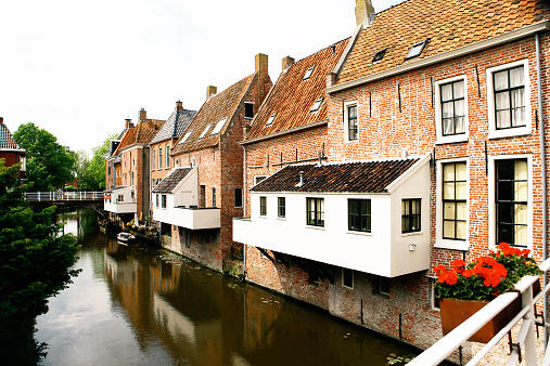 A beautiful, scenic image of red brick houses along a canal in Winsum, Groningen, the Netherlands. Popular floating kitchens are suspended over the water. 