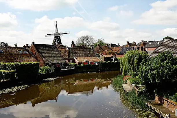 A scenic view of a windmill and houses along a canal in Winsum, Groningen, the Netherlands. 