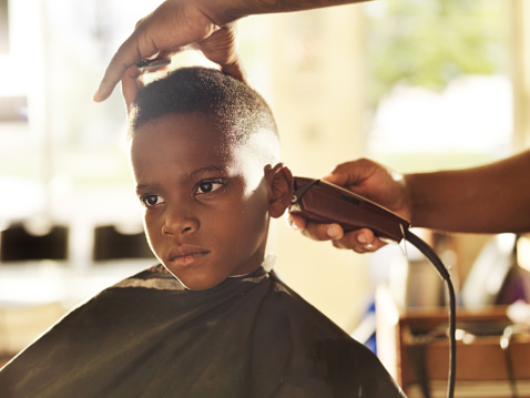 little boy getting his head shaved by barber with bored expression