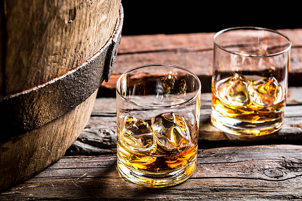 Two glasses of whiskey on the rocks beside an oak barrel Glass of whiskey in the old cellar. cognac region photos stock pictures, royalty-free photos & images