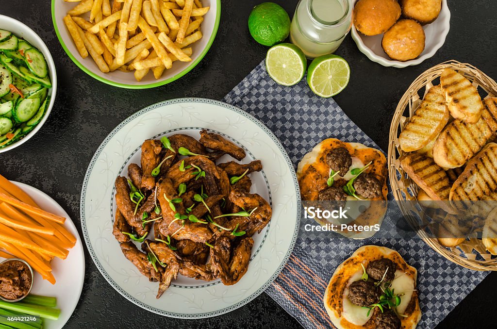 Sports feast - chicken wings, vegetable, french fries, pizza Chicken wings, vegetable, french fries, pizza, donuts, lime juice, dip, cucumber salad and toast. 2015 Stock Photo