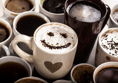 Lots of coffee in different cups with hearts and smile in one of them.