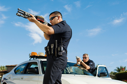 Side view of two police officers defending with gun against sky