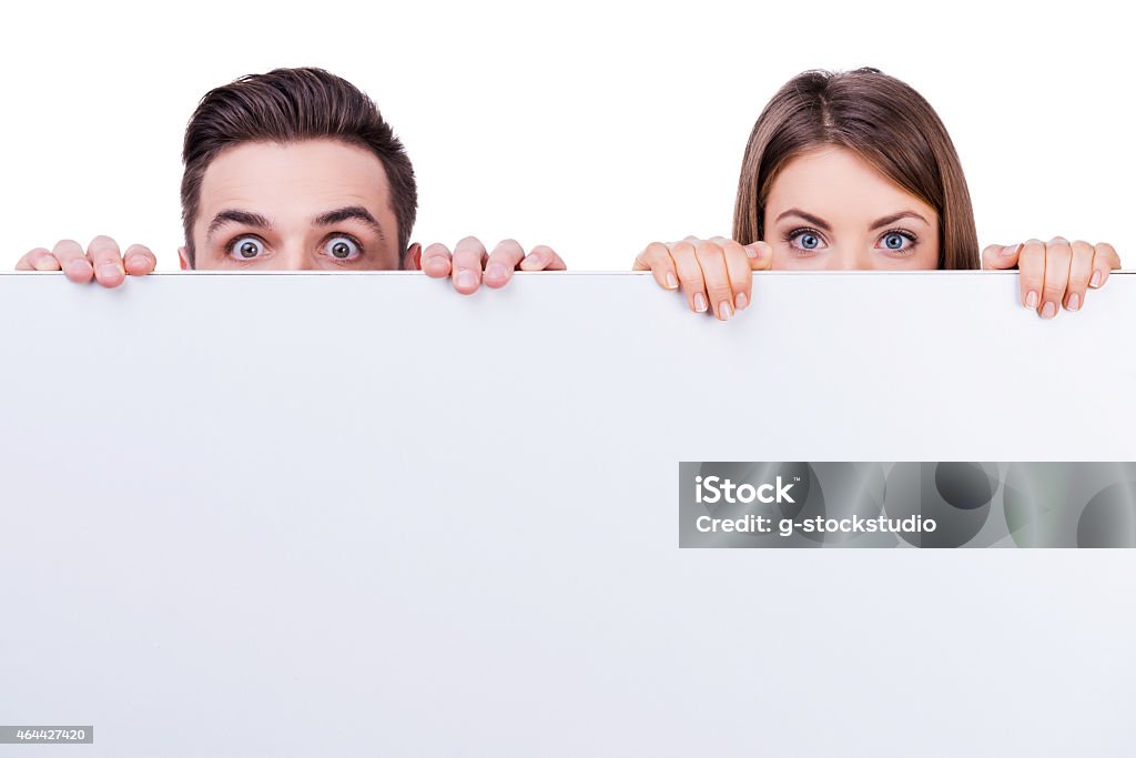 Behind the copy space. Beautiful young loving couple hiding behind copy space while standing against white background 2015 Stock Photo