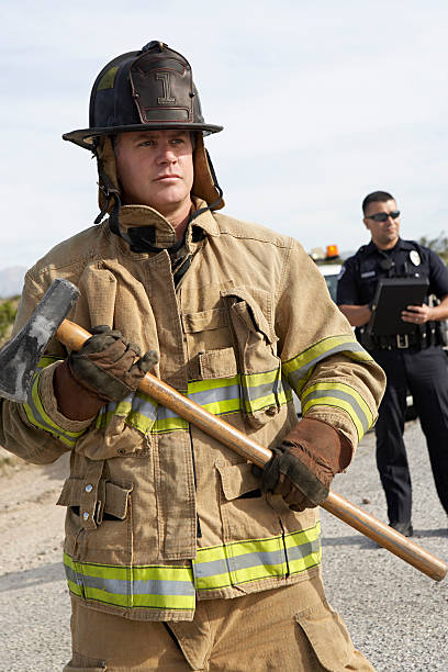 Firfighter at car crash Firefighter with axe, police officer in background police and firemen stock pictures, royalty-free photos & images