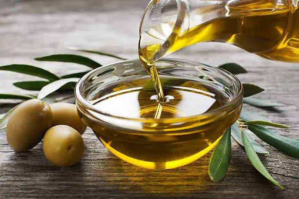 Bottle pouring virgin olive oil in a bowl close up