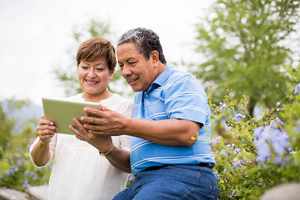 Happy senior couple with digital tablet Smiling senior couple using digital tablet in a park old woman smiling tablet stock pictures, royalty-free photos & images