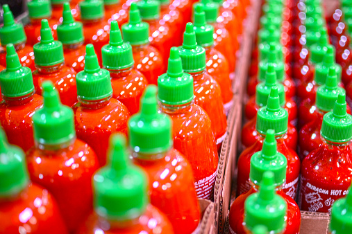 Haltom City, Texas, United States - February 20, 2015: A lot of Huy Fong's Rooster brand Thai hot sauce.  The bright red bottle, with green cap, lined up and ready to take on the world, one bottle at a time.  An American's favorite hot sauce.