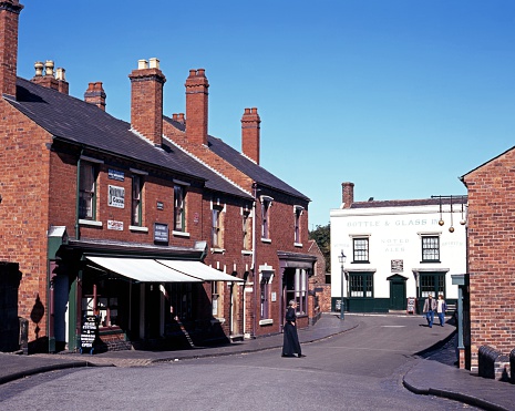 Dudley, United Kingdom - September 23, 1997: Victorian woman walking across the shopping street at the Black Country Living Museum with tourists to the rear, Dudley, West Midlands, England, UK, Western Europe.
