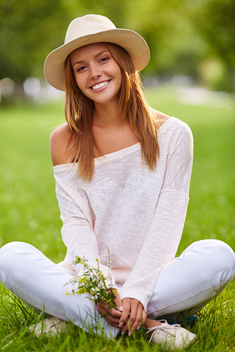 Stylish girl in hat and casualwear sitting on lawn in park