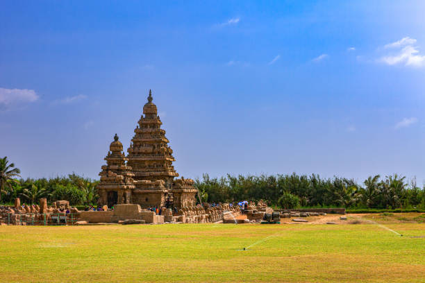 Mahabalipuram, India - January 30, 2015: Tourists at the Shore Temple. located on the shores of the Bay of Bengal, in Mahabalipuram or Mamallapuram, built in the 8th Century, between 700 and 728 AD, during the rign of the Pallava King Narasimhavarman II. Declared a UNESCO World Heritage site in 1984, the temple is one of the oldest structural temples in South India. It survived the Tsunamis of the 13th Century and 2004. Photo shot around noon against a blue sky with some clouds; people; copy space.