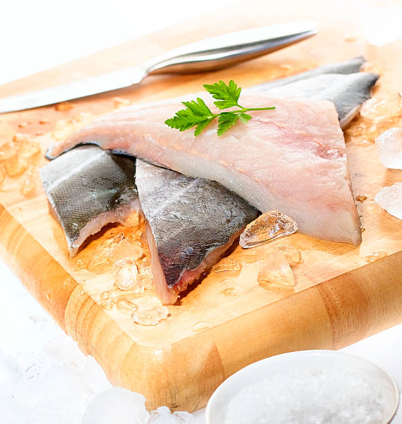Fresh white fish fillets on chopping board Fresh white fish fillets displayed on a chopping board with crushed ice, knife, cracked rock salt and parsley garnish  ocean perch stock pictures, royalty-free photos & images