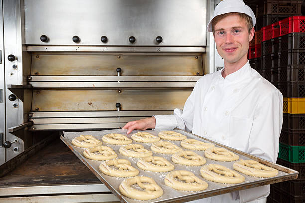 Baker in bakehouse or bakery presenting baking plate with pretzel dough