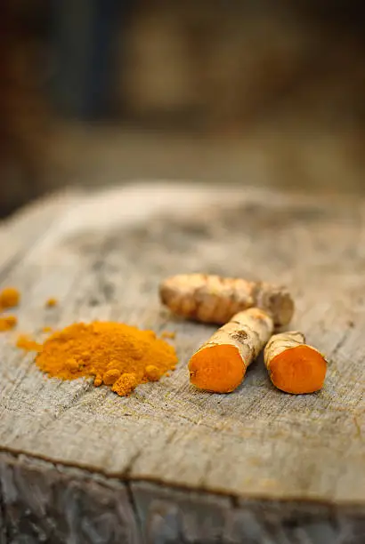 Turmeric root cut in half next to ground turmeric. Items placed on a natural wood setting.
