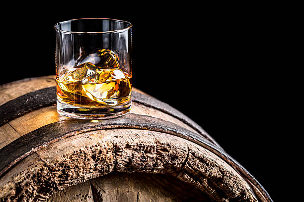 Glass of whisky with ice on old wooden barrel stock photo