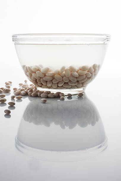 Soaked beans in a glass bowl and scattered beans on white with reflection