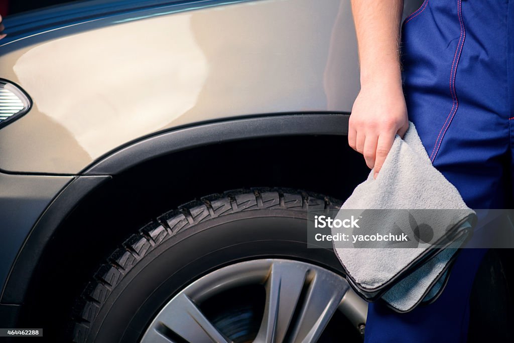 Car mechanic at the service station Welcome to our car service station. Closeup image of a handsome car mechanic in a uniform posing with a polishing wiper while standing against luxury suv in an authorized service station 2015 Stock Photo
