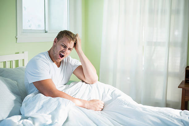 Young man sitting up in bad yawning