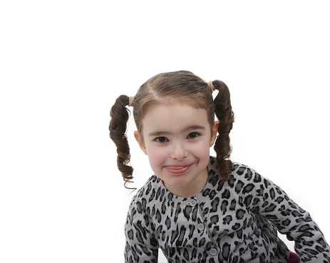 Portrait of a beautiful little 6 year old girl standing outdoors on the grass.  She has reddish blond hair, tied back in braids, blue eyes and freckles on her face.  She is smiling at the camera, wearing a light pink shirt.