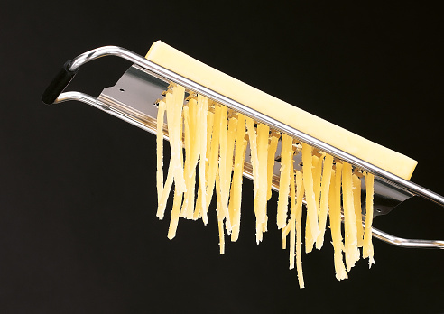 Cheddar cheese grating shown with hanging cheese shreds from grater isolated