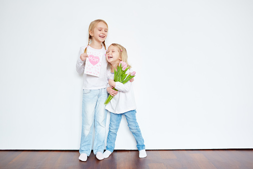 Laughing little sisters holding greeting card and tulip bouquet for their mother
