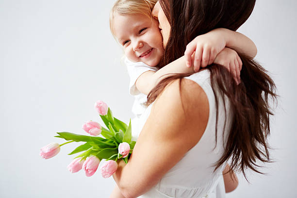 Cute little girl embracing warmly her mother holding tulips