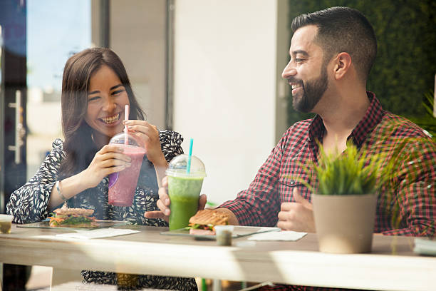 Having fun on a lunch date Cheerful young couple having lunch and healthy smoothies at a juice bar juice bar stock pictures, royalty-free photos & images