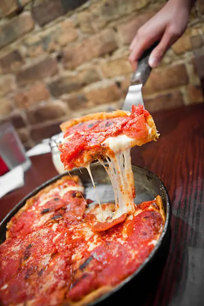 Chicago deep dish pizza being served from whole pizza with cheese dripping down.