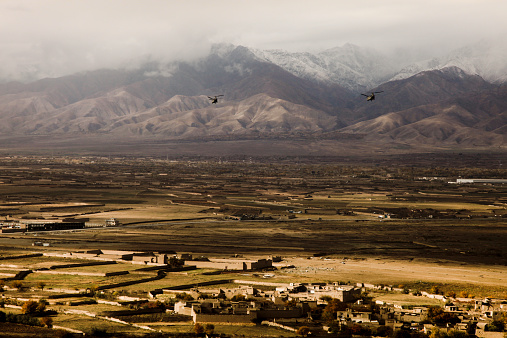 US Army CH-47 Chinook helicopters flying over Afghanistan showing unique Afghani architecture in valley below with harsh snow covered mountains in the background. Shot with Canon 5D MKII.