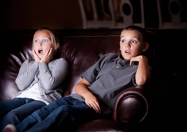 Two children on the couch acting shocked by the television stock photo