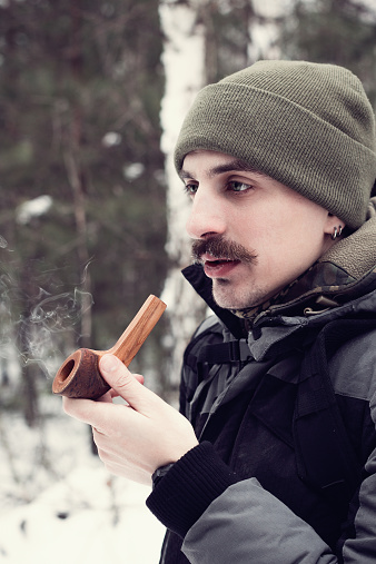 Mustached man smoking a pipe in winter forest