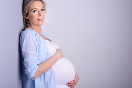 beautiful forty years old pregnant woman with blue shirt isolated on a gray background