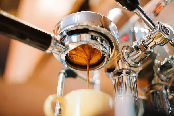 Freshly ground morning espresso coffee pouring through the bottomless portafilter of a coffee machine