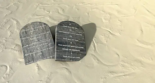 Two stone tablets with the ten commandments inscribed on them lying on brown desert sand