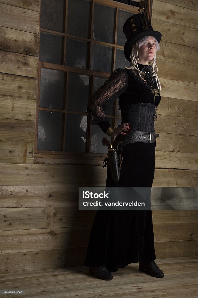 Steampunk Gunfighter Outside An Old Cabin Portrait of a blonde Steampunk shootist girl with dreadlocks. 1870-1879 Stock Photo