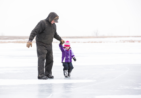 Little girl holding Grandpa's hand as they walk on the frozen lake.