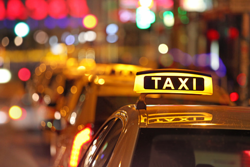 Close up of illuminated sign of yellow taxi cars waiting in line at night, with defocused street lights in the background. City life and street traffic with colorful street signs photographed in Berlin.
