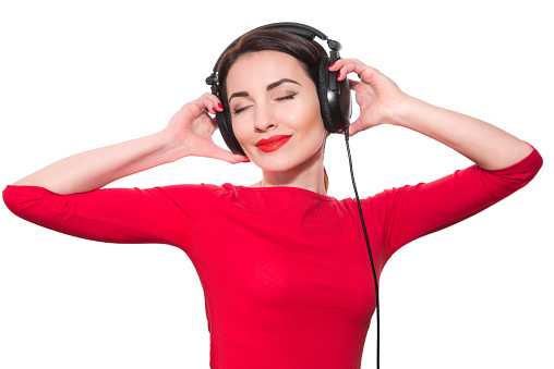 Portrait of mid adult man standing against bright red background, holding his blazer on the shoulder and scrolling through his playlist on smart phone while listening to music via headphones.