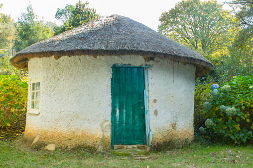 Rustic traditional rondavel with a green door and a thatch roof in a country setting