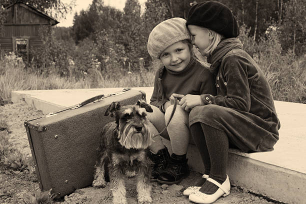 Two young girls with dog at bus stop Girls tell each other secrets, sitting at the bus stop suitcase luggage old fashioned obsolete stock pictures, royalty-free photos & images