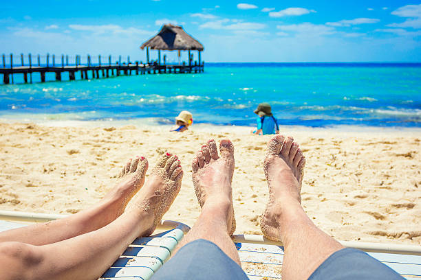 Couple watching their kids playing on the beach on vacation Sandy toes and feet of a couple on lounge chairs enjoying a beach vacation while watching their kids play in the sand. Tropical resort setting cozumel photos stock pictures, royalty-free photos & images