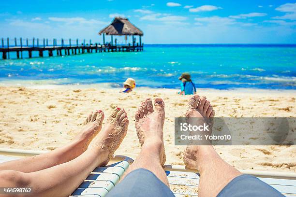Couple Watching Their Kids Playing On The Beach On Vacation Stock Photo - Download Image Now