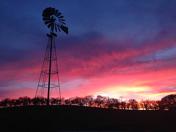 istock Windmill and trees in silhouette against a colorful sunset. 464619094